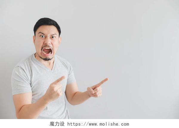 亚洲男子在灰色T恤与手点在空旷空间的愤怒的脸.
